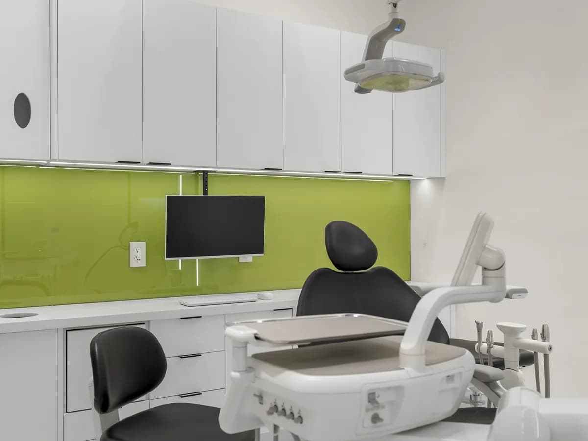 A treatment room with an olive-green glass backsplash and chairside monitor