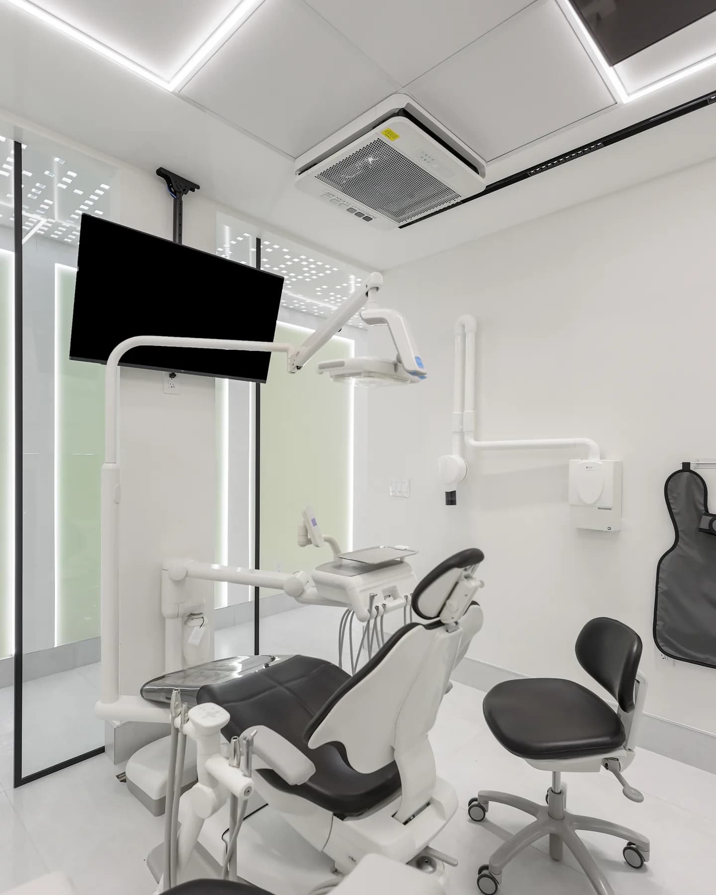 A treatment room at Allo Dental Clinic seen past its glass partition, chair and overhead screen ready