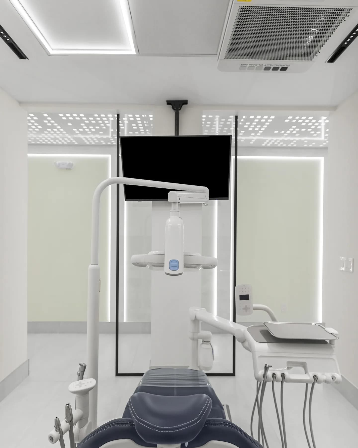 A dental chair centred beneath the overhead screen in a treatment room at Allo Dental Clinic